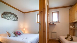 Un dormitorio con cama, mesita de noche, lámpara, ventana y estante con un osito de peluche.