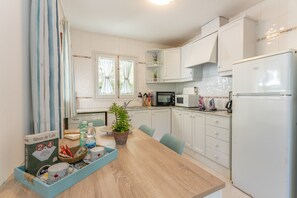 Moderni keittiö, jossa on valkoiset kaapit, mikroaaltouuni, jääkaappi sekä ruokapöytä, jonka päällä on kasvi ja tarjoilualusta, jossa on erilaisia esineitä.