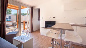 Eine moderne Küche mit Essbereich, einem Fernseher und einem Balkon mit Blick auf ein parkendes Auto und Grünflächen.