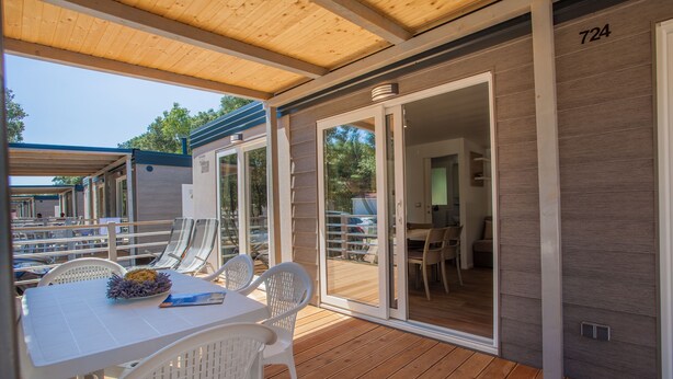 Ein überdachter Außenbereich mit Tisch und Stühlen, einer Holzterrasse und einer Schiebetür zu einem Innenraum.