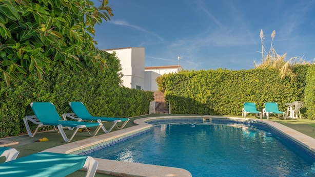 A swimming pool with lounge chairs, surrounded by greenery and a white building. - Beautiful Holiday Apartment “Apartamento Delfín 2” with Pool, Terrace & WiFi; Parking Available in the Street (Cala Blanca)
