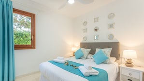 A hotel room with a bed, a nightstand, a lamp, a window with curtains, and wall decorations. - Beautiful Holiday Apartment “Apartamento Delfín 2” with Pool, Terrace & WiFi; Parking Available in the Street (Cala Blanca)