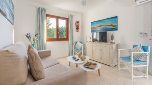 A living room with a sofa, chairs, a coffee table, a TV, and a painting on the wall. - Beautiful Holiday Apartment “Apartamento Delfín 2” with Pool, Terrace & WiFi; Parking Available in the Street (Cala Blanca)