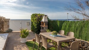 Un patio con tavolo e sedie, un barbecue, una pianta in vaso e vista sul mare.