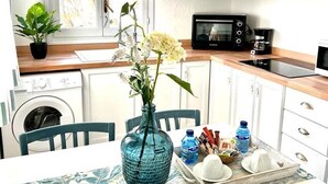 Una cucina compatta con mobili bianchi, un forno a microonde, una lavatrice e un'area pranzo con un tavolo apparecchiato per due.