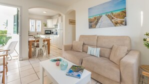 Un soggiorno con un divano beige, un tavolino da caffè bianco e un quadro raffigurante una spiaggia.