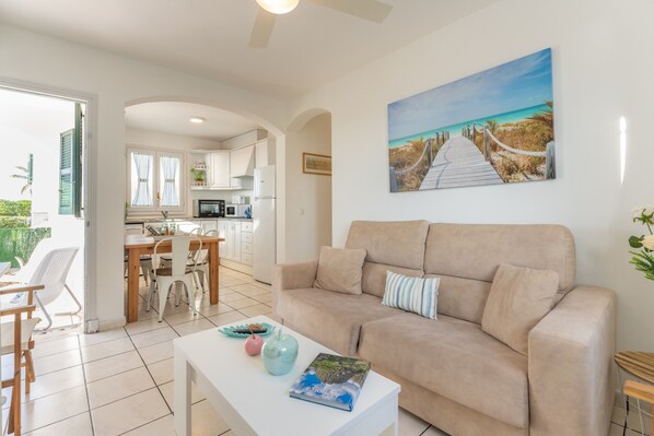 A living room with a beige sofa, a white coffee table, and a painting of a beach scene.