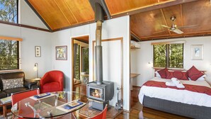 Una habitación moderna con una mesa de vidrio, sillas rojas, cama con ropa de cama roja, techo de madera y una estufa de leña.