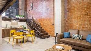 A modern kitchen with a brick wall, a dining area with yellow chairs, and a brown leather sofa with blue cushions. - Art Loft 05 'The Mechanic' in Valencia (València)