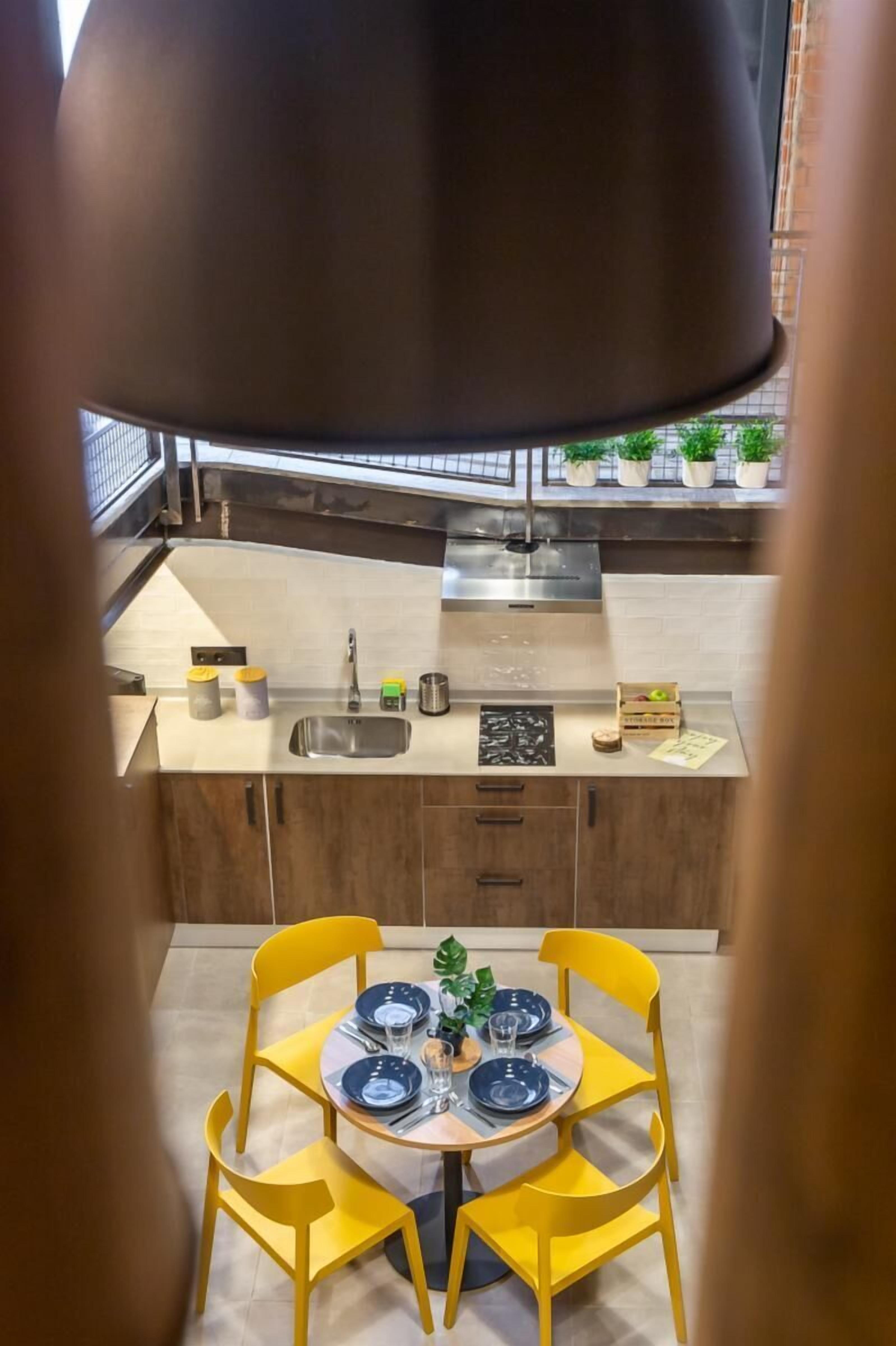 Une cuisine moderne dotée d’un îlot central, d’un évier et d’un coin repas avec des chaises jaunes et une table dressée pour deux personnes.