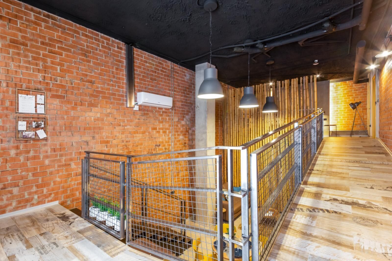 Un interior moderno con paredes de ladrillo visto, suelo de madera, barandillas de metal e iluminación colgante.