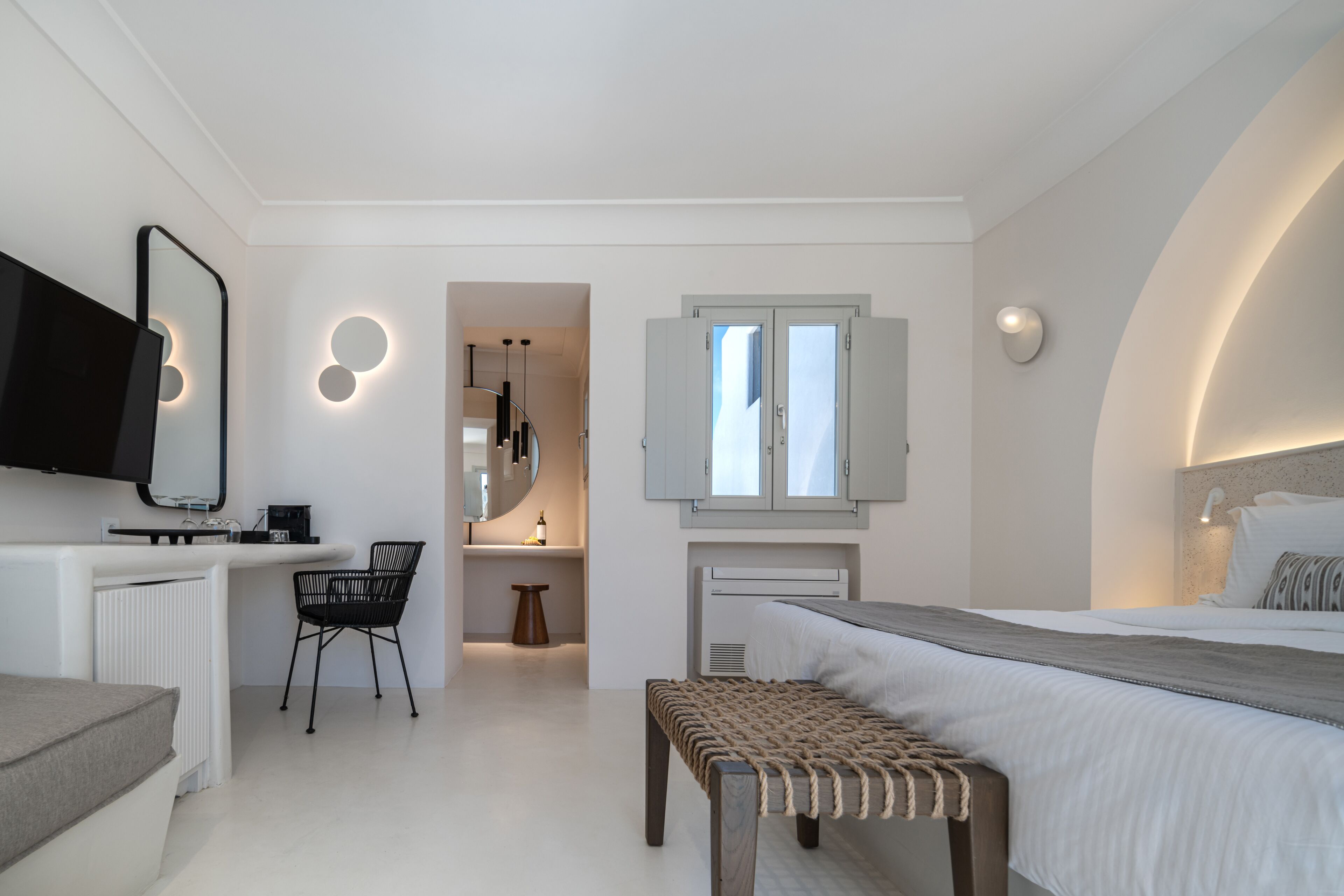 Una camera da letto moderna con un letto, un comodino, una TV e un piccolo angolo relax.