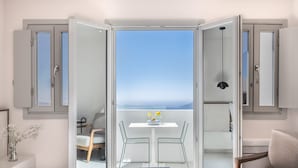 A bedroom with a bed, a small table with a vase of flowers, and a balcony with a table and chairs. - Akra Suites & Spa (Santorini)