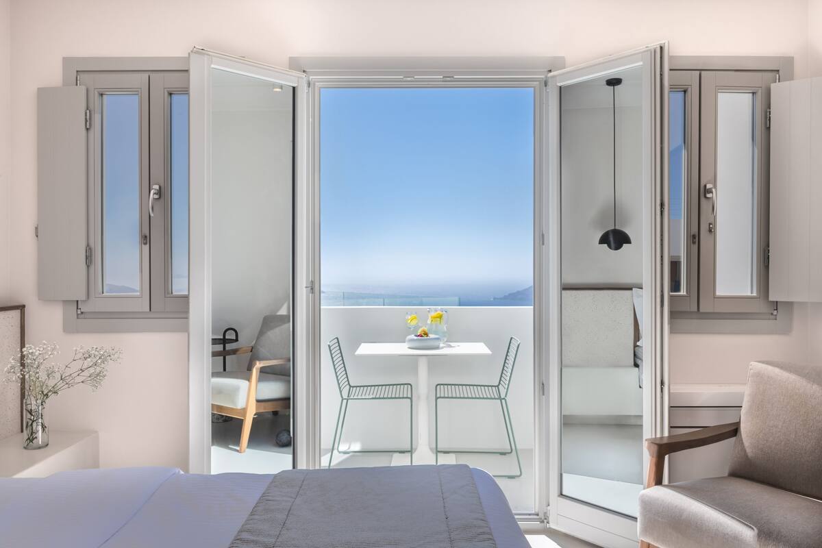 A bedroom with a bed, a small table with a vase of flowers, and a balcony with a table and chairs.