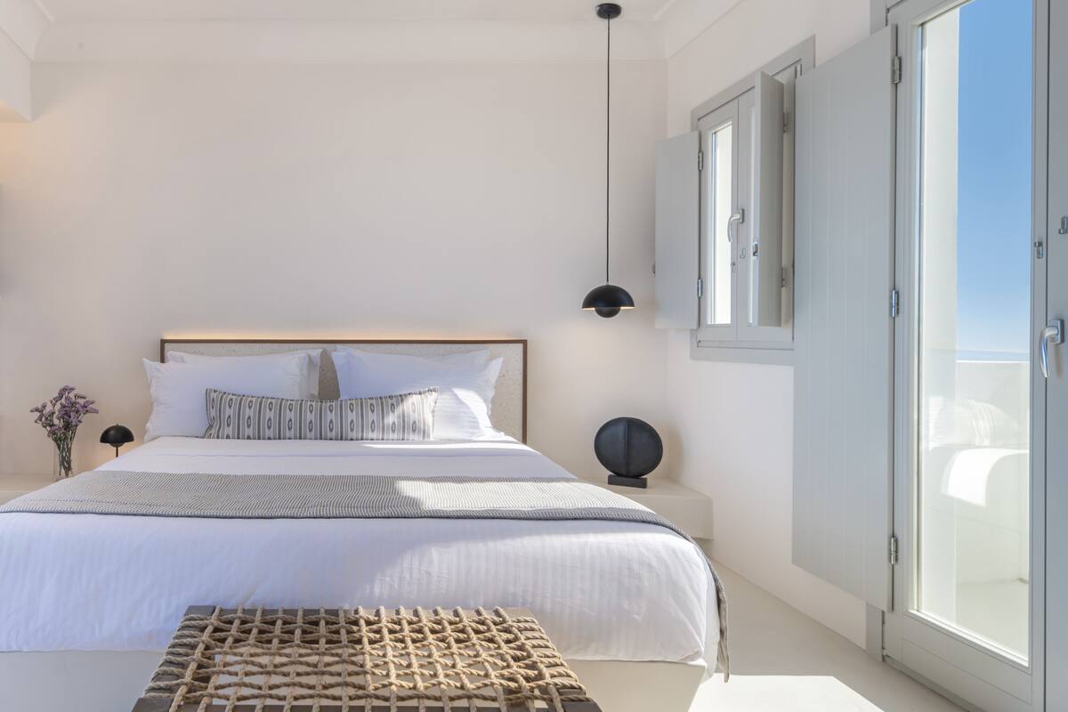 A modern bedroom with a large bed, a bedside table, a hanging light, and a sliding glass door to the outside.