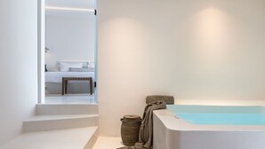A modern bathroom with a bathtub, a wicker basket, and a towel on a shelf. - Akra Suites & Spa (Santorini)