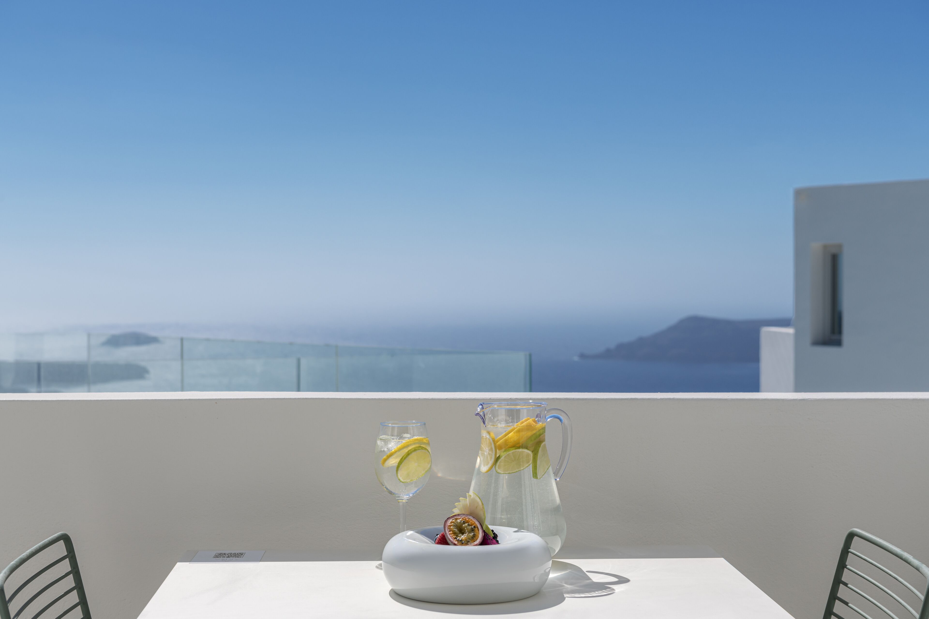 A table with a pitcher and two glasses on a balcony with a clear view of the sea.