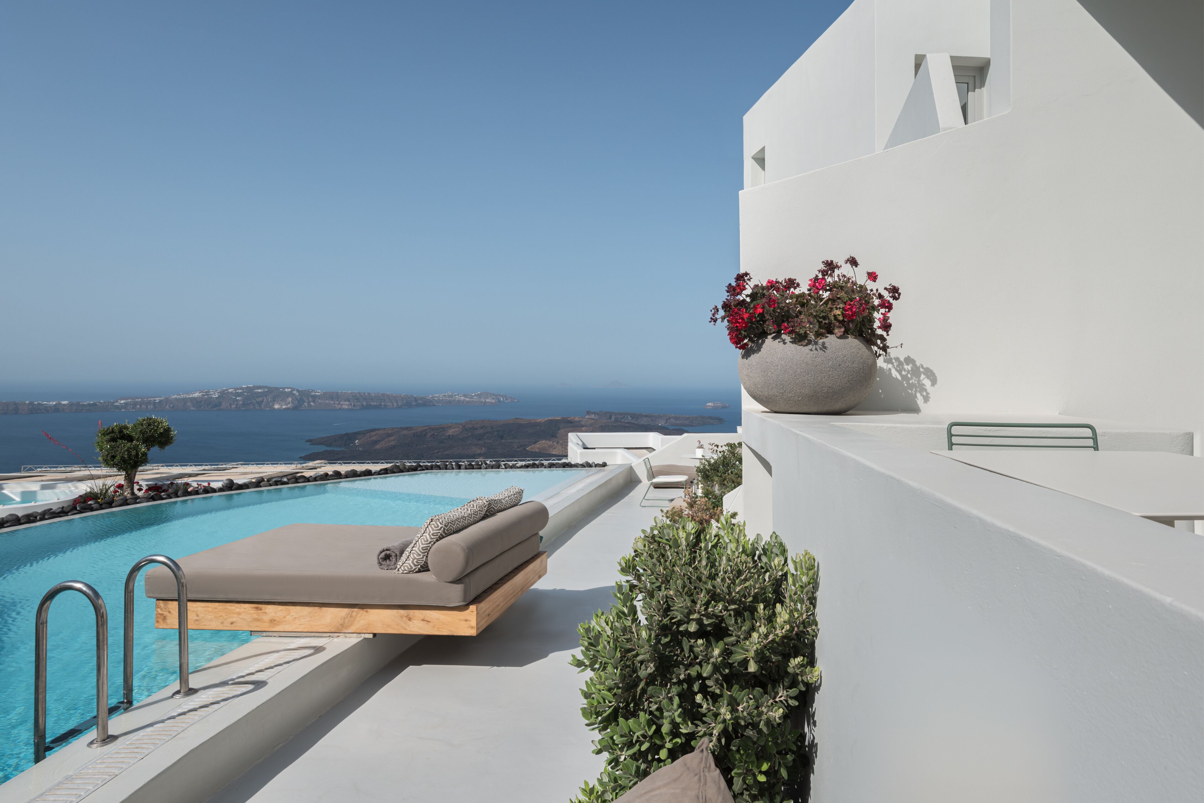 A modern pool area with a lounge chair and a large planter with flowers, overlooking a scenic view.