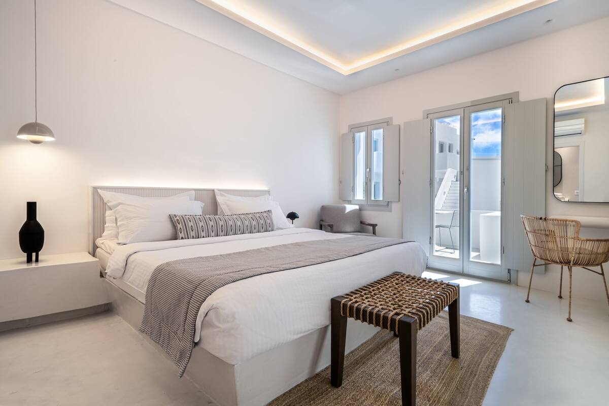 A modern bedroom with a large bed, bedside tables, a bench, and a chair.