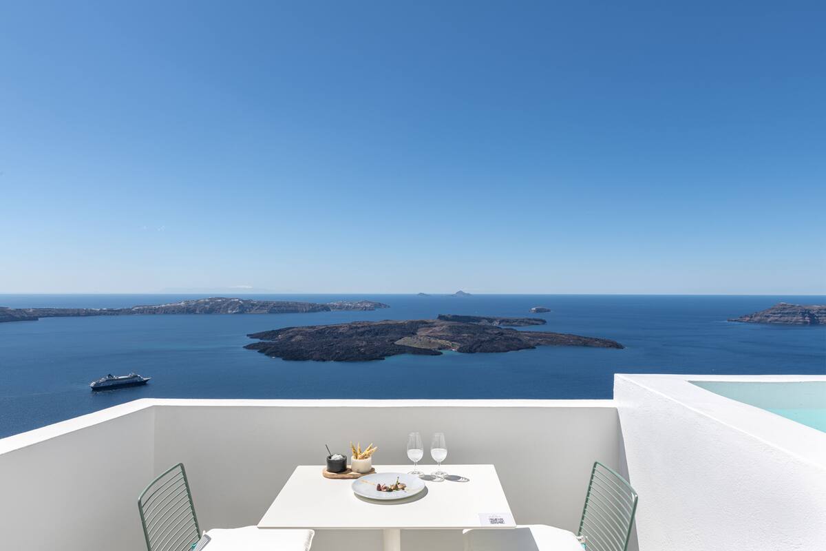 A table with a meal and glasses on a balcony overlooking a sea with islands.