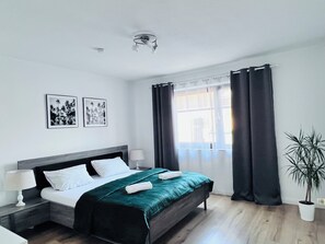 A modern hotel room with a bed, two bedside tables, a window with curtains, and two wall-mounted pictures. - Modern Apartment with a Terrace, 15 Minutes from Downtown, NETFLIX (Dinslaken)