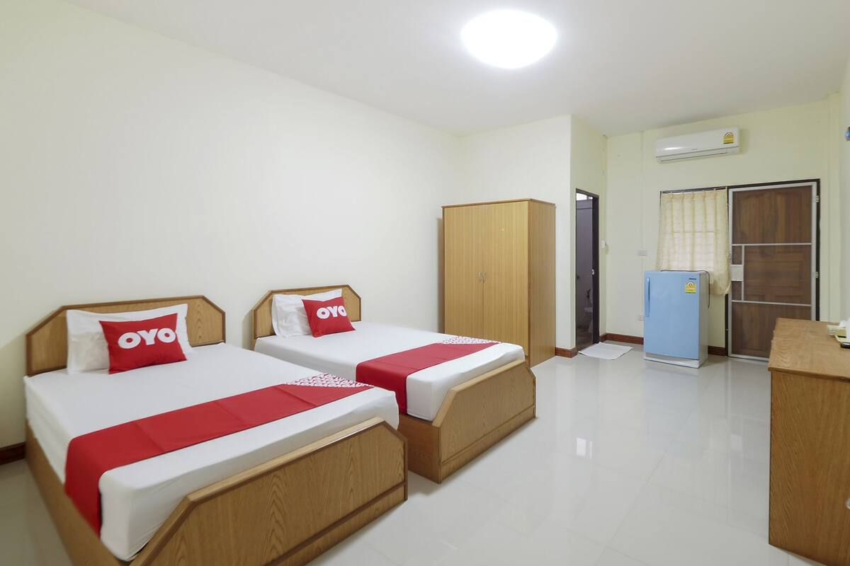A hotel room with two beds, a wardrobe, a desk, and a refrigerator.