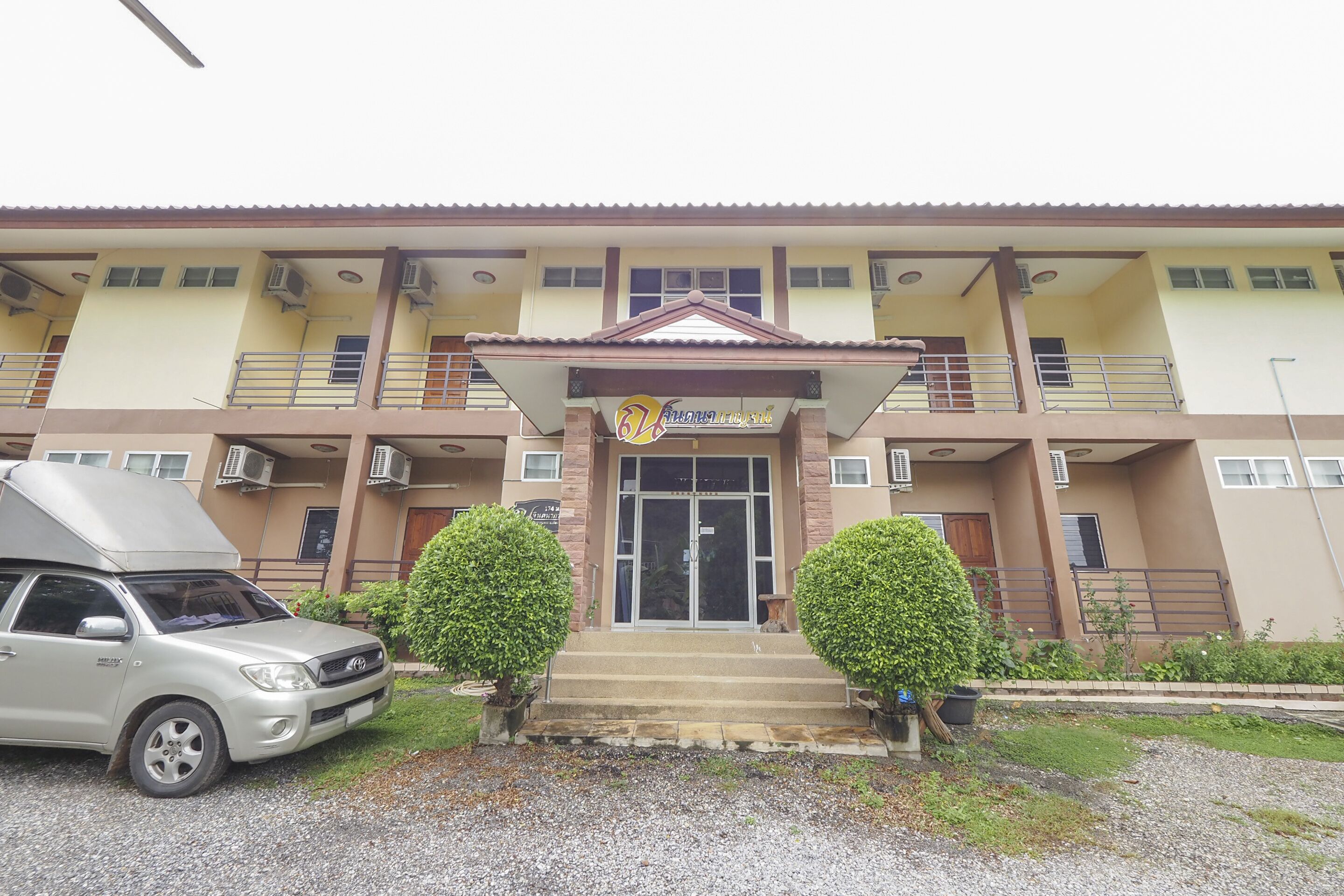 A multi-story building with a central entrance, air conditioning units, and a parked car.