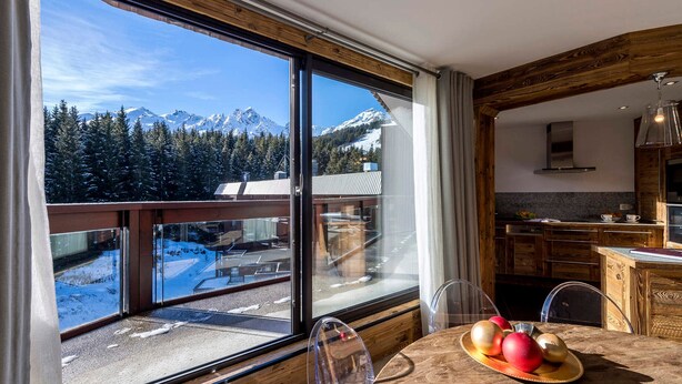 Una cocina moderna con armarios de madera y un amplio ventanal con vistas a un paisaje montañoso nevado.