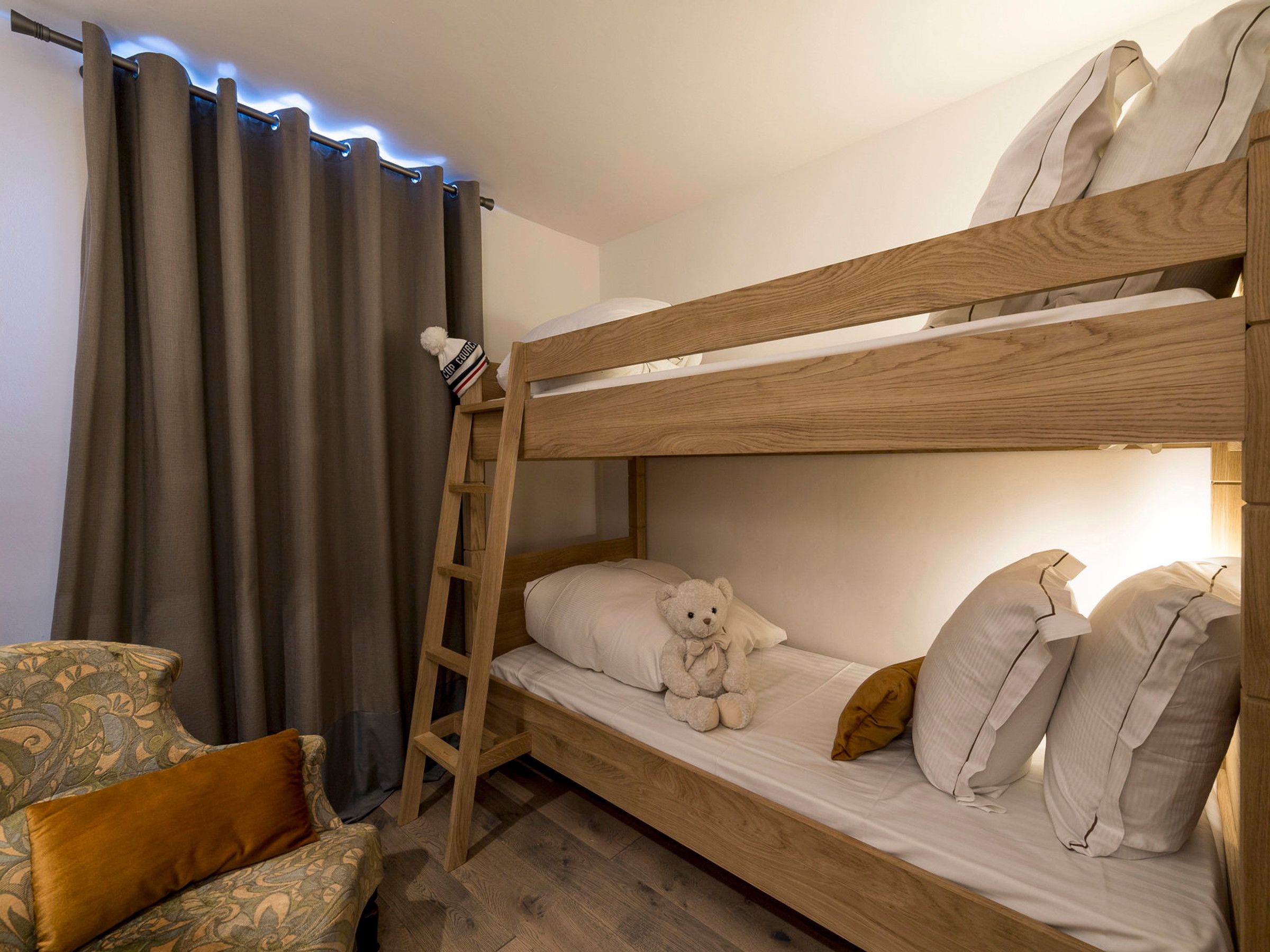 Una cama litera con escalera, un oso de peluche y una almohada en la cama inferior.