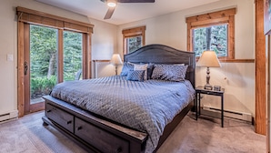 A bedroom with a large bed, two bedside tables with lamps, a ceiling fan, and large windows with wooden frames. - Relaxed Comfort in a Prime Location – The Pines at Ore House! (Steamboat Springs)