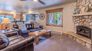 A living room with a stone fireplace, leather sofas, a wooden coffee table, and a ceiling fan. - Relaxed Comfort in a Prime Location – The Pines at Ore House! (Steamboat Springs)