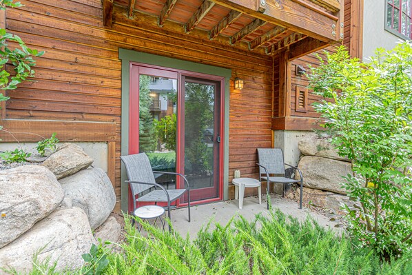 A wooden cabin with a glass door, two chairs, and a small table outside. - Powder Day Retreat | Fireside + Shuttle (Steamboat Springs)