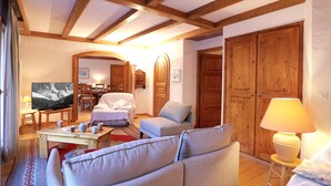 A cozy living room with wooden beams, a sofa, a television, and a dining area with a table and chairs. - Spacious 3-bedroom, ski-in/ski-out with parking and wifi (Courchevel 1550)