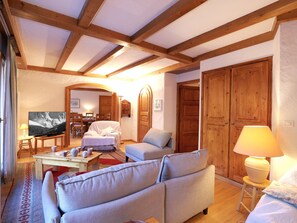 Ein gemütliches Wohnzimmer mit Holzbalken, einer Couch, einem Fernseher und einem Essbereich mit Tisch und Stühlen.