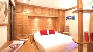 A bedroom with wooden cabinets, a bed with red pillows, a nightstand, and a reading lamp. - Spacious 3-bedroom, ski-in/ski-out with parking and wifi (Courchevel 1550)