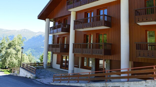A multi-story wooden building with balconies, large windows, and a view of mountains. - Spacious 3-bedroom, ski-in/ski-out with parking and wifi (Courchevel 1550)