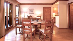 A dining room with a wooden table and chairs, a painting on the wall, and a door leading to another room. - Spacious 3-bedroom, ski-in/ski-out with parking and wifi (Courchevel 1550)