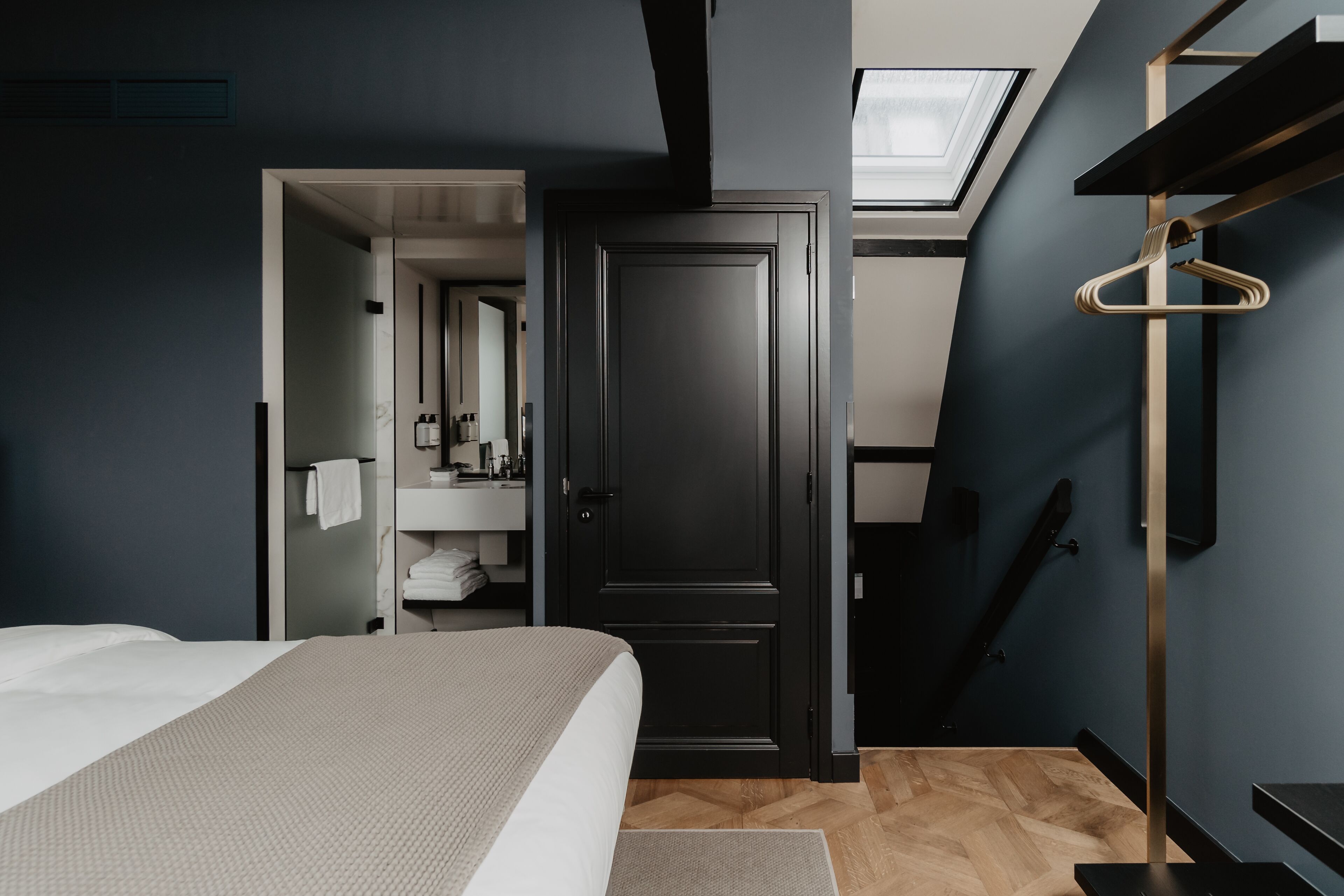 A modern hotel room with a large bed, a walk-in closet, a skylight, and a wooden floor.