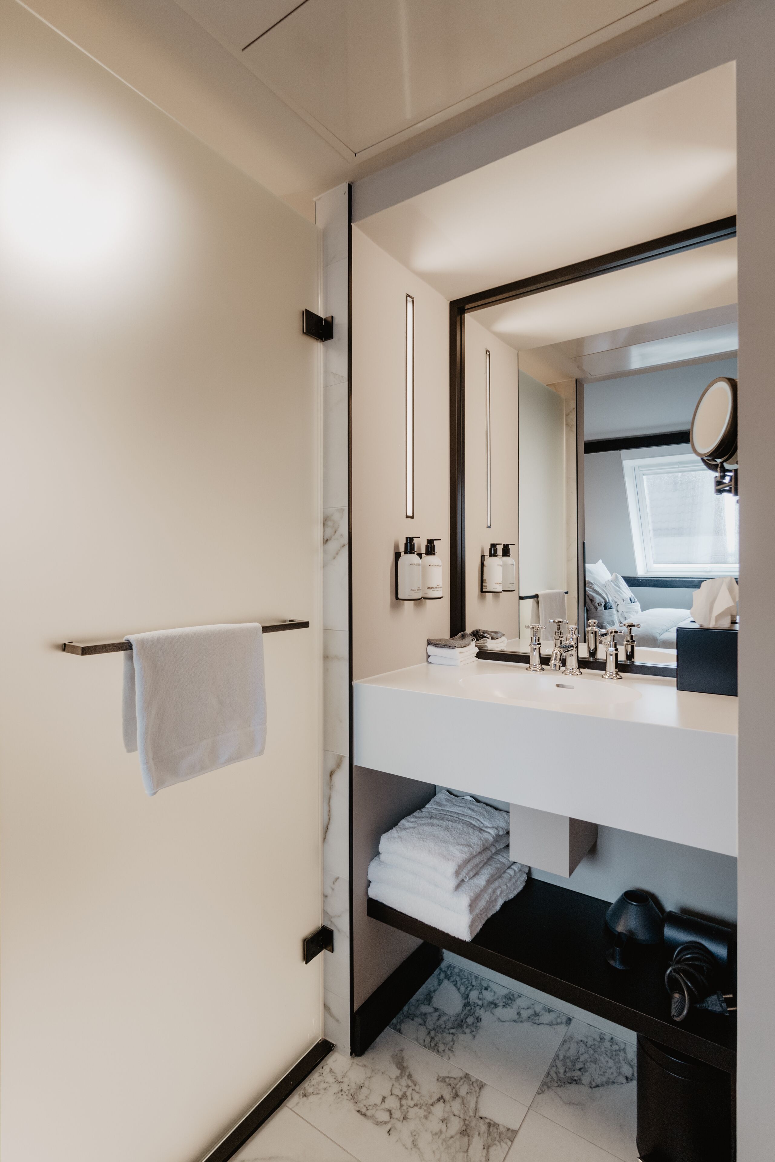 Un baño moderno con tocador blanco, un espejo grande y un perchero para toallas.