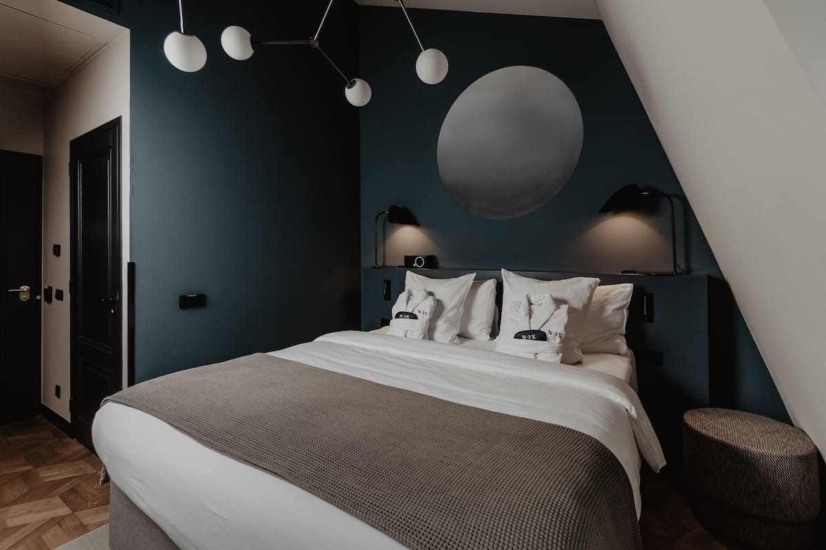 Ett modernt sovrum med en stor säng, en sfärisk vägglampa och en mörkblå accentvägg.