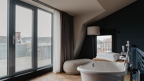 Un baño moderno con una bañera independiente, un ventanal con cortinas y vistas a la ciudad.