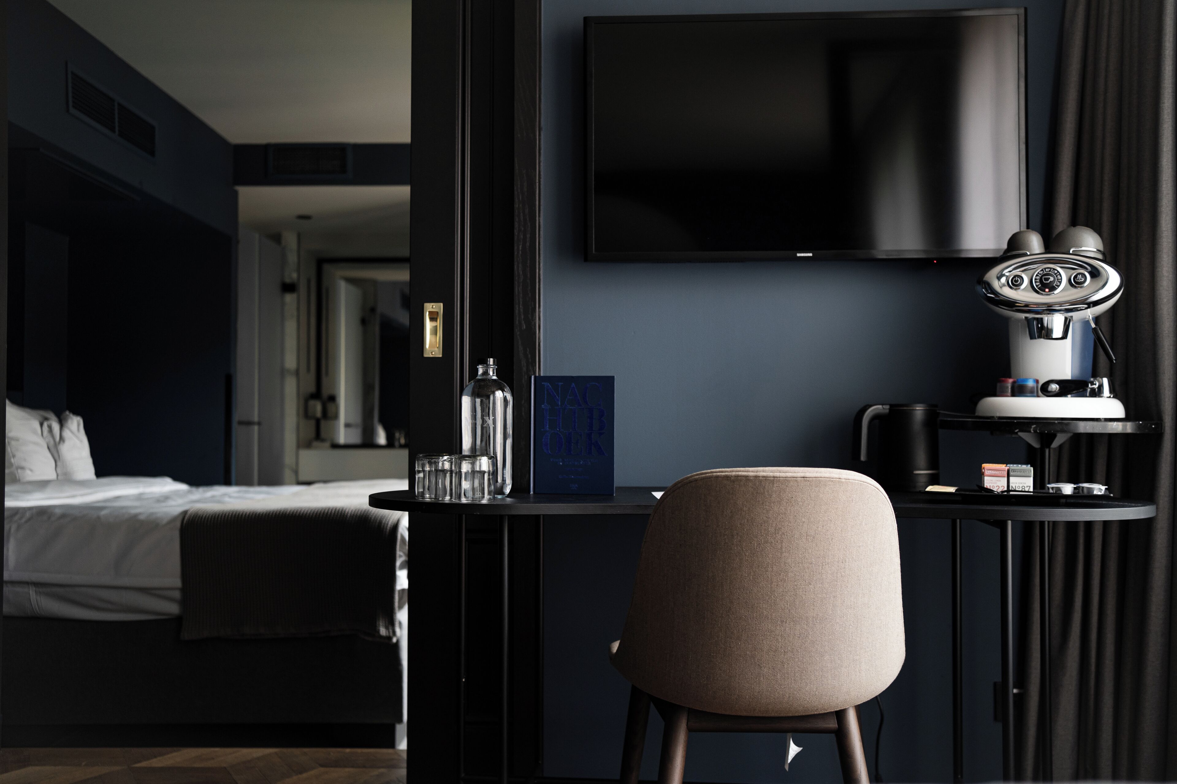 A hotel room with a bed, a desk with a chair, a television, and a minibar.