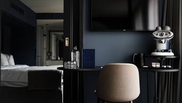 A hotel room with a bed, a desk with a chair, a television, and a minibar.