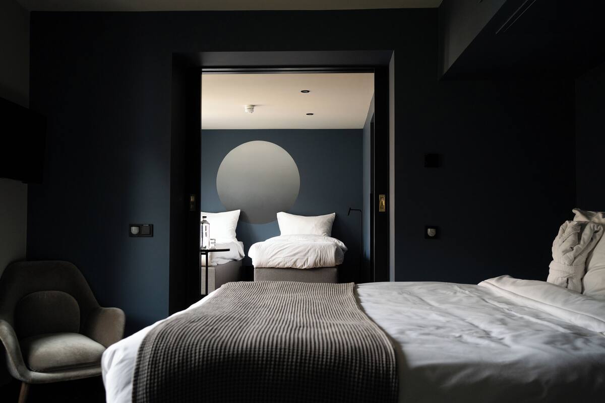 Ett modernt hotellrum med en stor säng, en stol och ett skrivbord med en lampa.