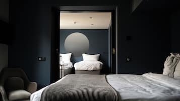 A modern hotel room with a large bed, a chair, and a desk with a lamp.