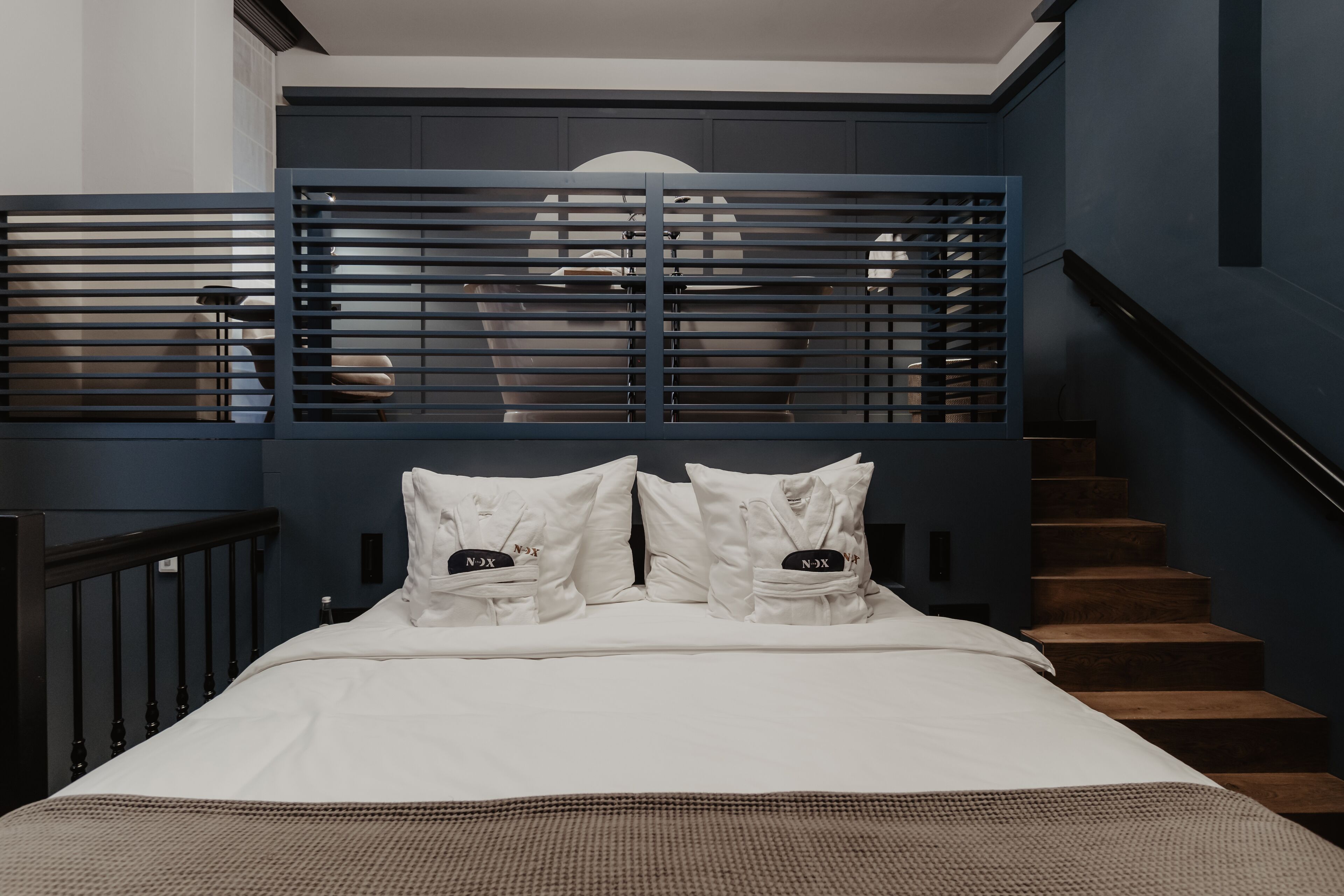 Un dormitorio con una cama, almohadas blancas, una pared azul oscuro y una escalera.