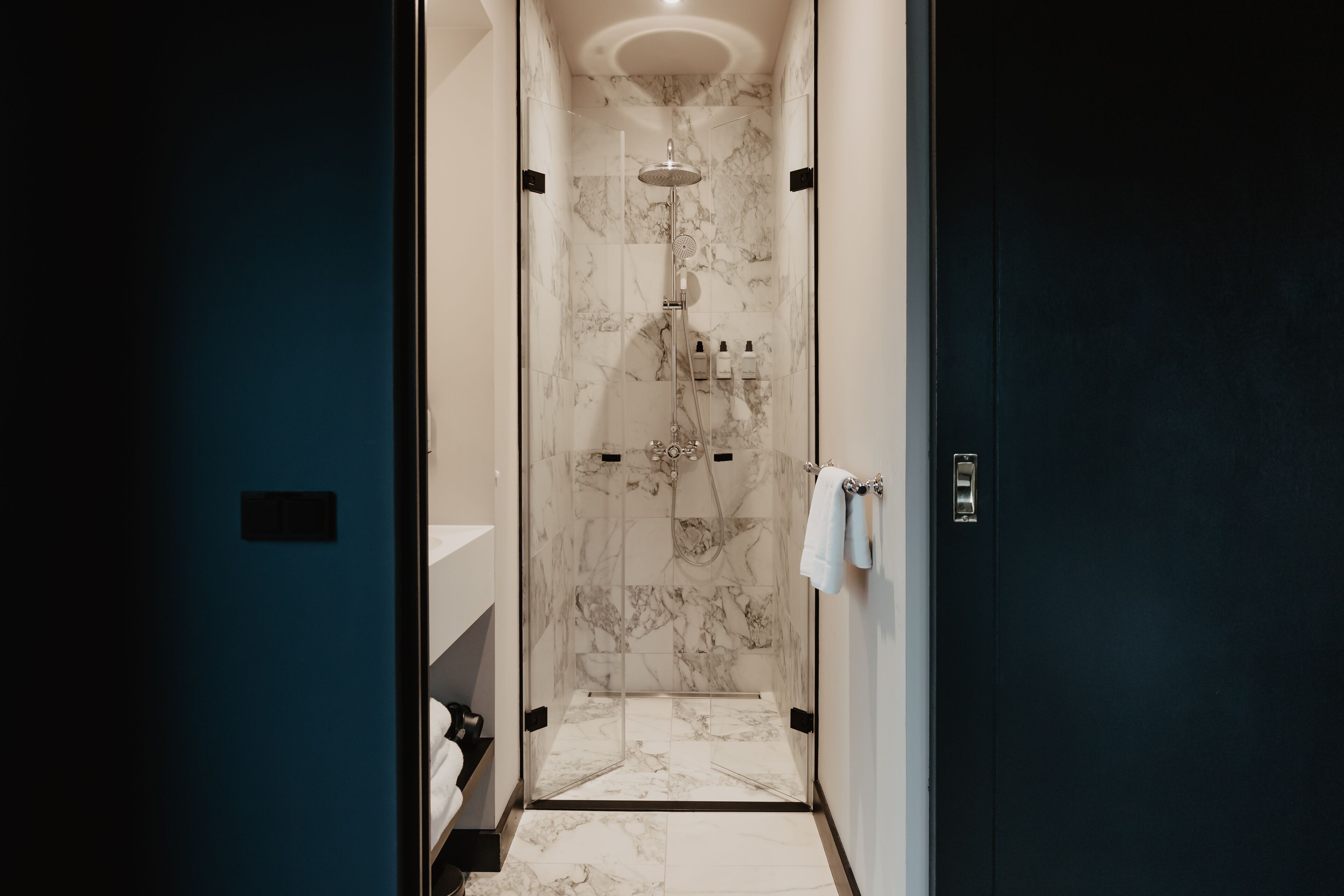 Une salle de bain moderne avec une douche à parois de verre, des murs en marbre et une porte sombre.