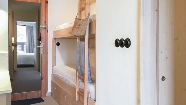 Une petite pièce avec un lit superposé, un petit bureau et une porte dotée d’un trou de serrure.