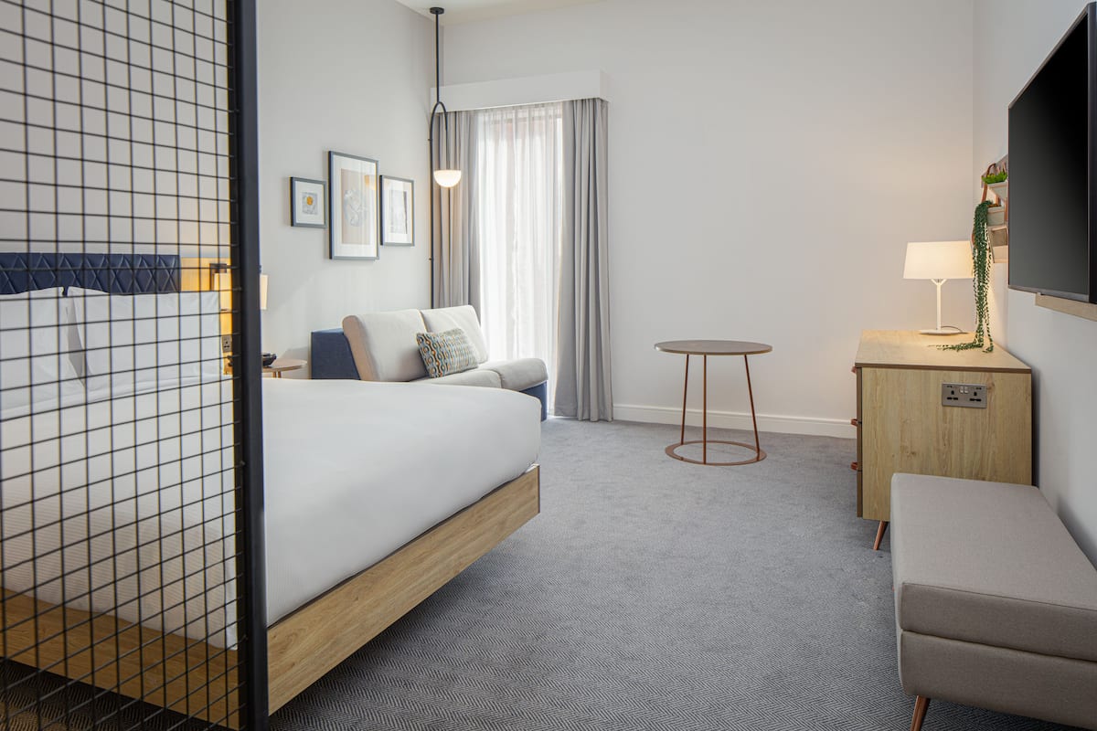 Een hotelkamer met een bed, een bank, een eettafeltje, een televisie en een bureau.