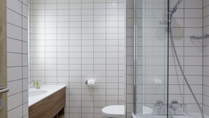 Een moderne badkamer met een douchecabine van glas, een wit toilet en een houten wastafelmeubel met een wastafel.